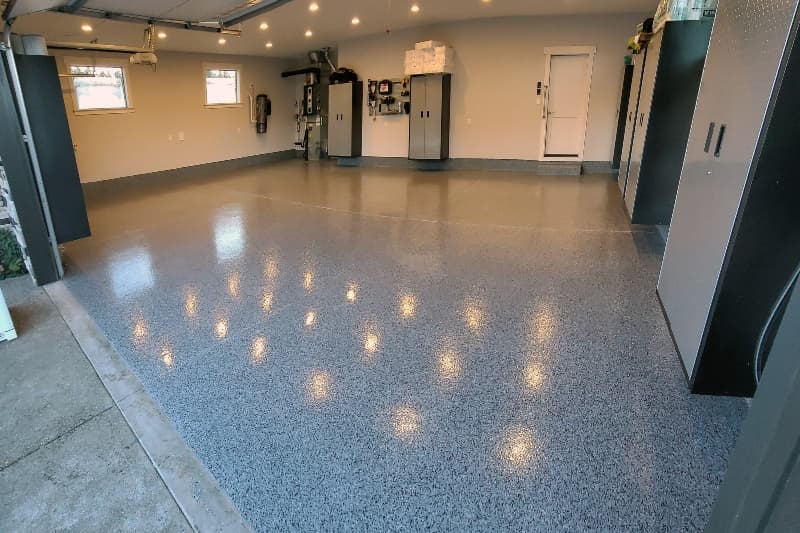 Glossy dark grey flake garage floor reflecting ceiling lights, with storage cabinets along the walls.