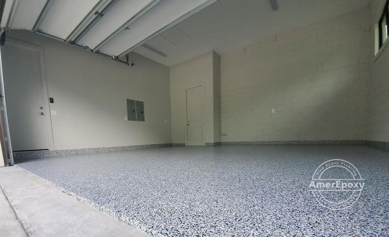 Low-angle view of a grey and white flake garage floor extending from the driveway into an empty garage.