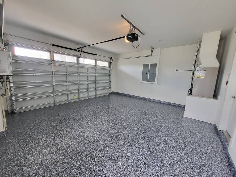 Empty garage with a grey, black and white flake floor, white walls, and a closed garage door.