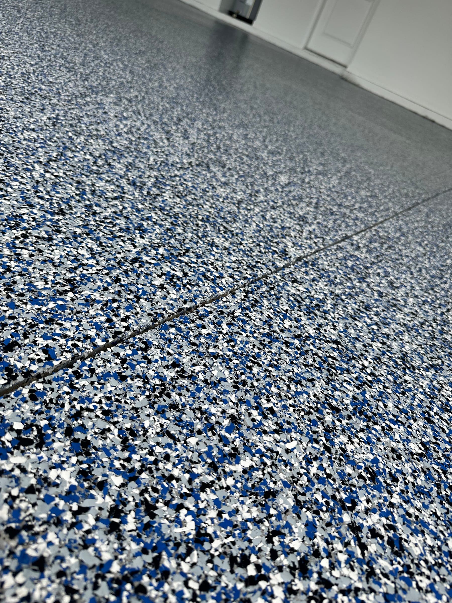 Close-up of a blue, black, white and grey flake epoxy garage floor with a saw-cut joint running across it.