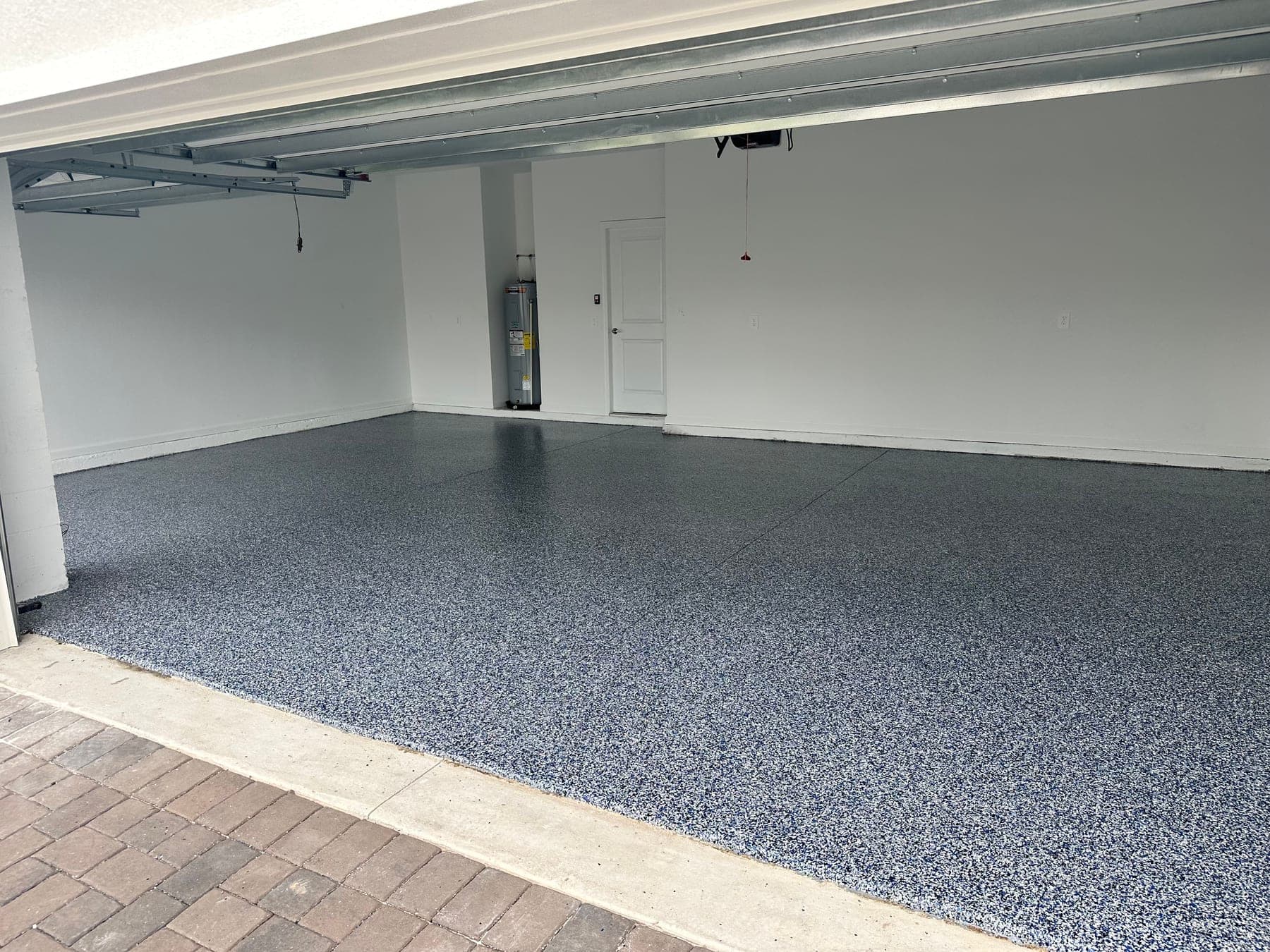 Two-car garage with a grey, blue and white flake epoxy floor, white walls, and brick pavers in the foreground.