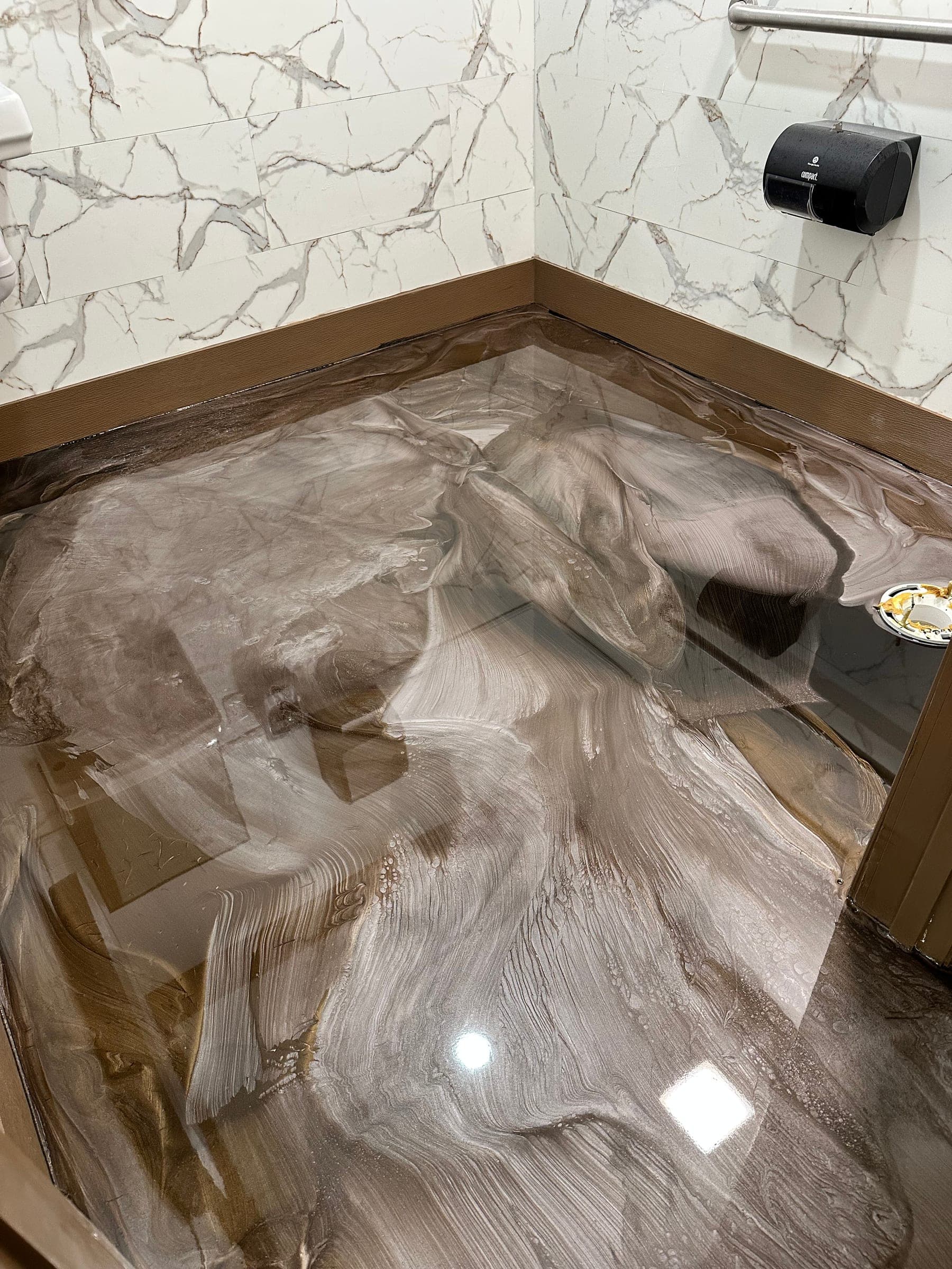 Grey, white and brown marbled metallic epoxy floor in a commercial restroom corner, with a paper dispenser on the wall.