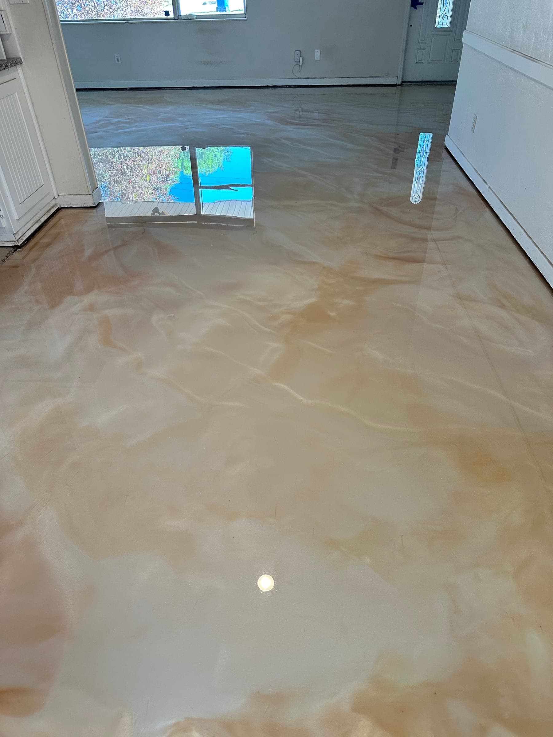 Glossy tan and cream metallic epoxy floor running from a home's kitchen entry toward the front room, with a window reflected in it.