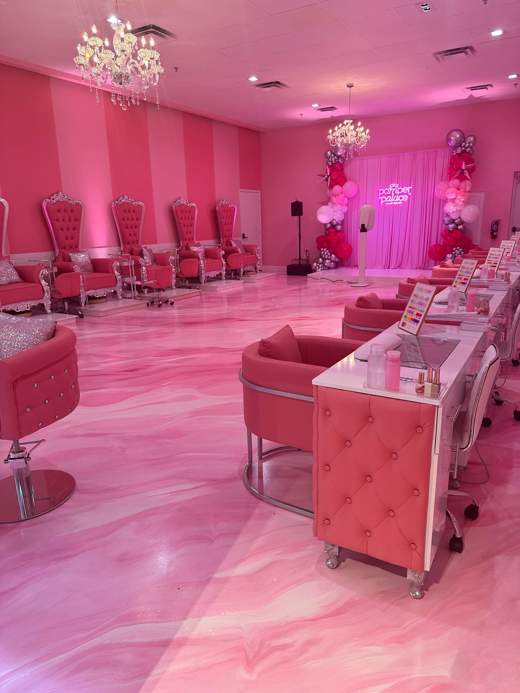 Pink and white marbled metallic epoxy floor in a nail salon, with pink throne chairs, chandeliers and a balloon arch.