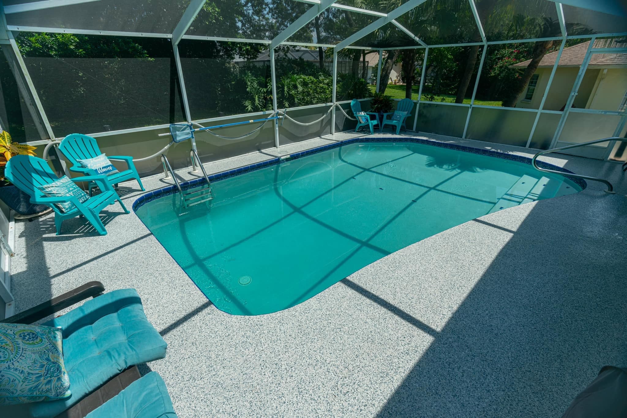 Light grey speckled deck surrounding a screened swimming pool with turquoise chairs.
