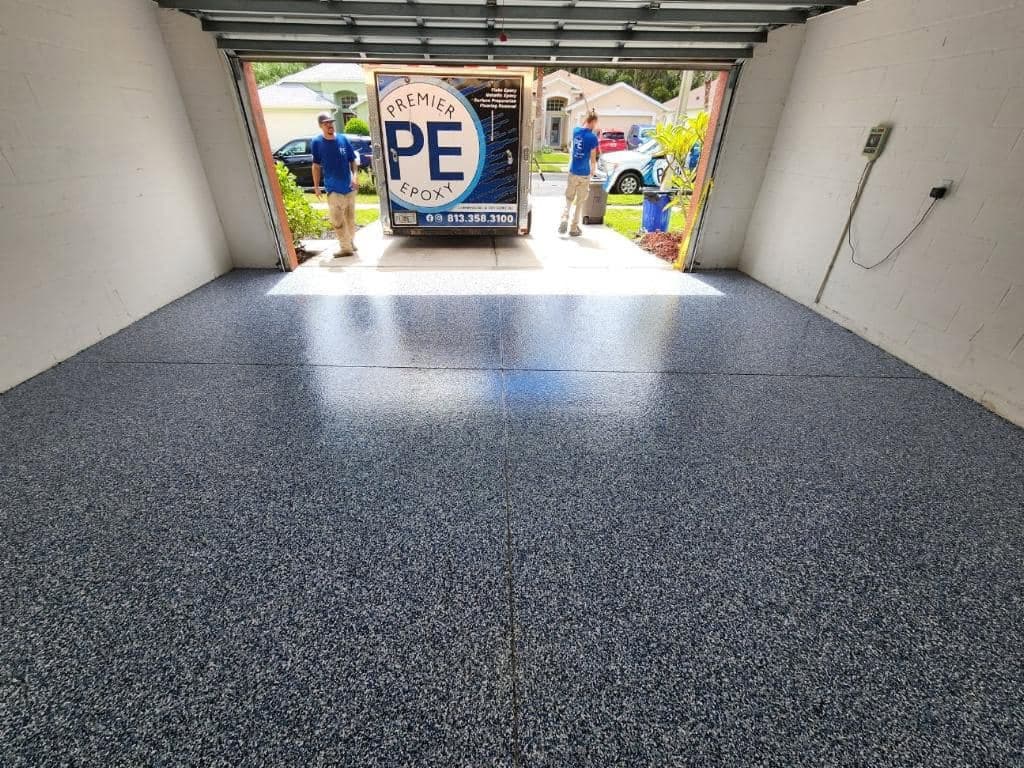 Dark grey and white flake garage floor with a Premier Epoxy trailer visible through the open door.