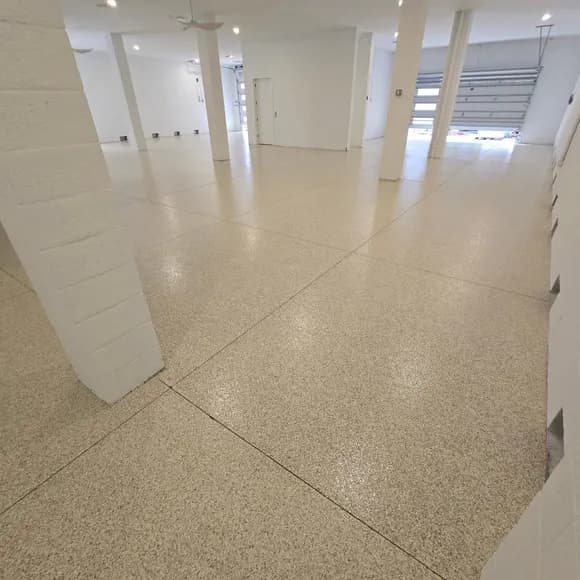 Cream-coloured speckled floor with straight control joints in a bright interior with white columns and garage doors.