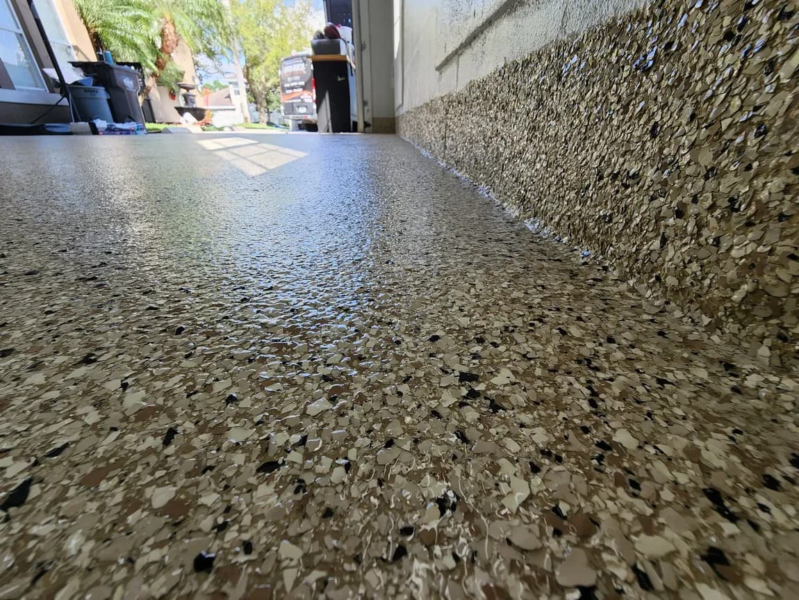 Close-up of a tan, brown, black and white flake garage floor with a matching coated wall base.